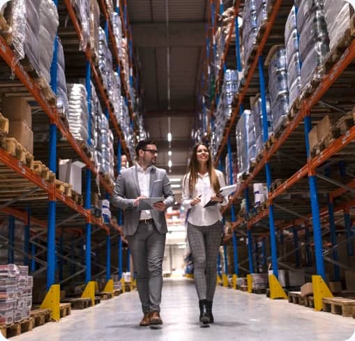 Two staff reviewing stock between tall racks in a warehouse