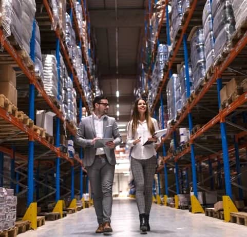 Two staff reviewing stock between tall racks in a warehouse
